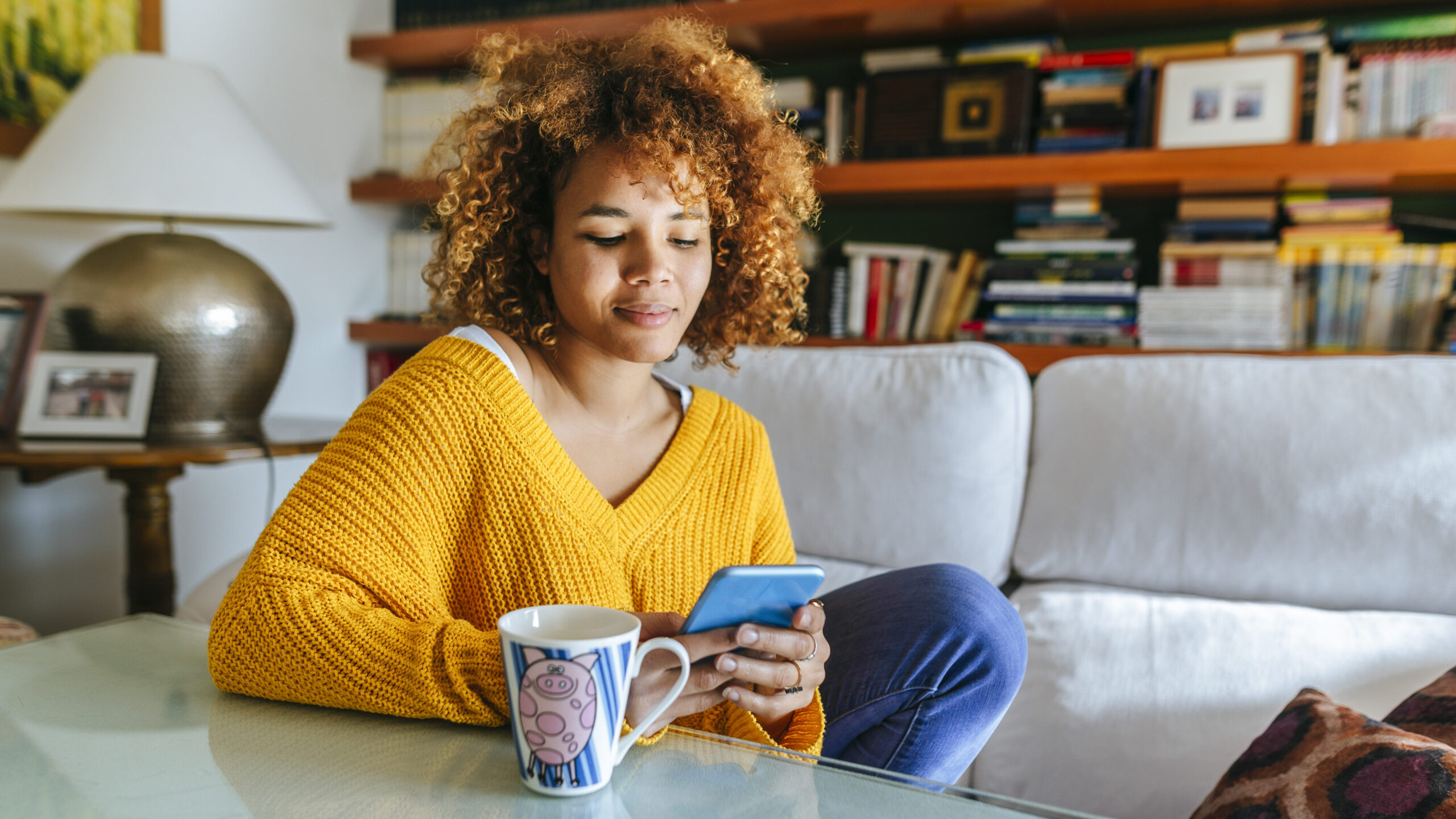 Young woman looks at her mobile phone while sitting on her sofa at home.