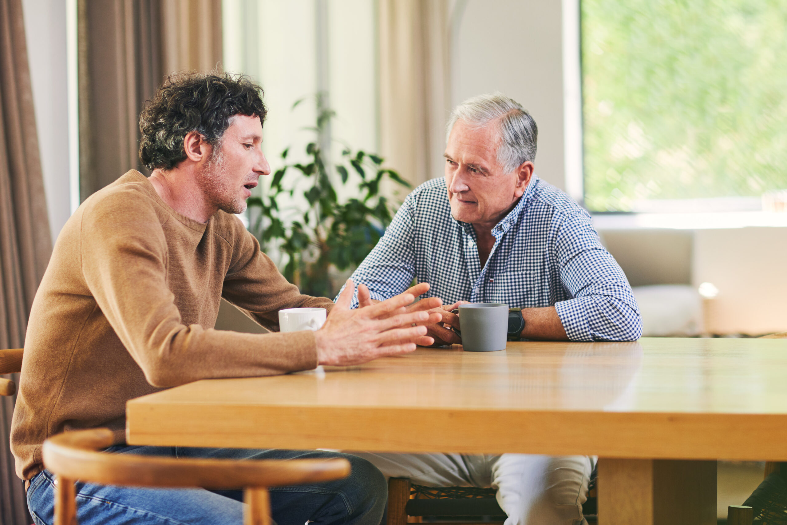 Young man and older man sitting and engaging in conversation in a house.
